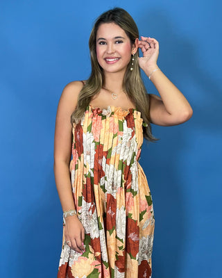 A woman modeling a strapless floral maxi dress with a ruffled neckline