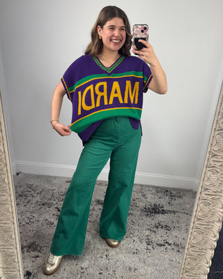 Person wearing a colorful sweater with 'Mardi' text, green pants, and gold shoes in a room.