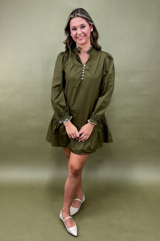 Woman wearing a green dress with long sleeves on a matching background