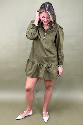 Woman wearing an olive green dress with a plain background