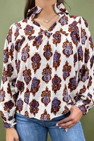 Person wearing a patterned blouse with long sleeves and blue jeans against a green background
