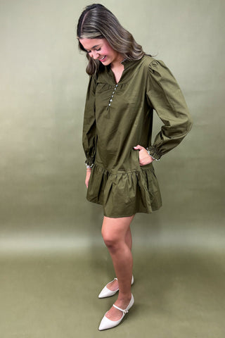 Woman wearing an olive green dress with a plain background