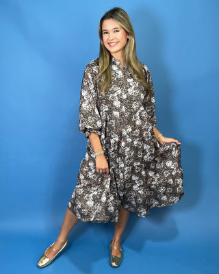 A woman modeling a brown and white floral print midi dress with three-quarter sleeves