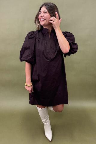 Woman wearing a black dress with puffed sleeves and white boots on a green background