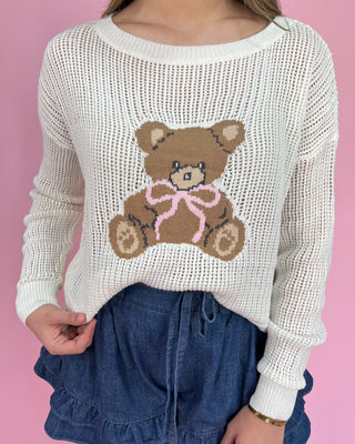 Woman wearing a white sweater with a teddy bear design on a pink background