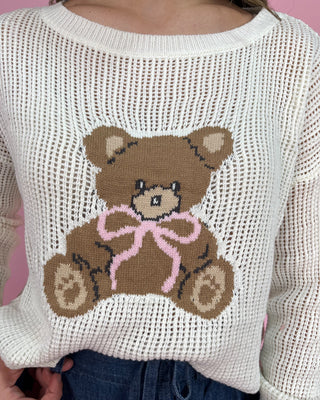 Woman wearing a white sweater with a teddy bear design on a pink background