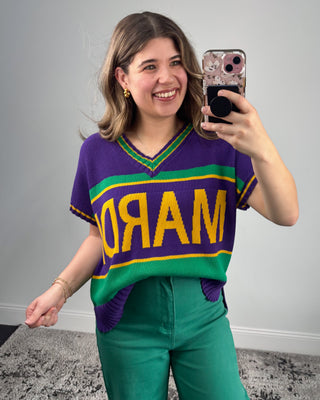 Person wearing a colorful sweater with 'MARDI GRAS' text, taking a selfie.