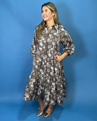 A woman modeling a brown and white floral print midi dress with three-quarter sleeves and a button-up front