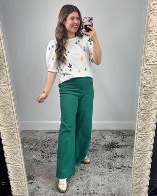 Woman taking a mirror selfie wearing a floral top and green pants.