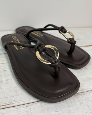 Black sandals with gold rings on a light wooden surface
