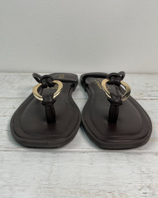 Pair of black sandals with gold rings on a light wooden surface