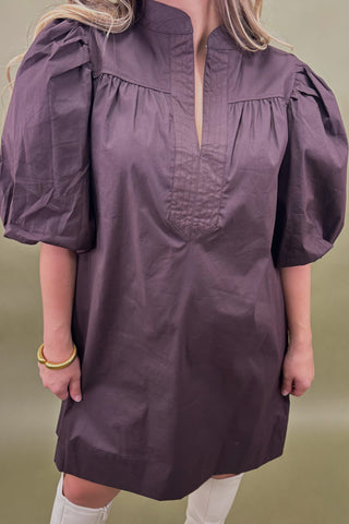 Person wearing a purple dress with puff sleeves against a green background