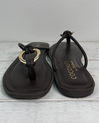 Black sandals with gold accents on a light wooden surface