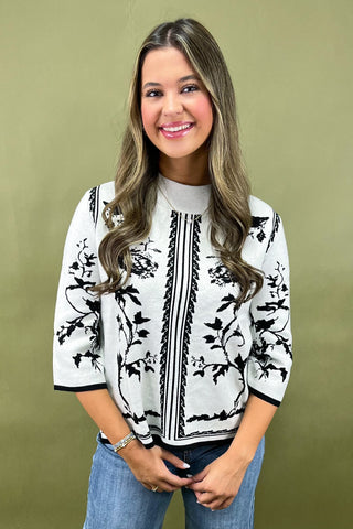 Woman wearing a white blouse with black floral patterns against a green background