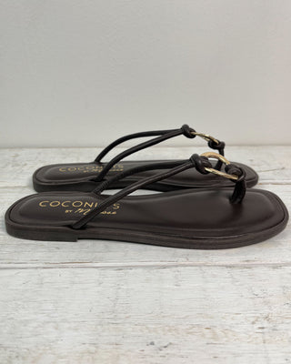 Black sandal with a gold buckle on a light wooden surface