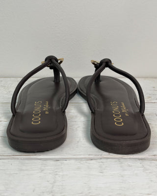 Pair of black sandals with 'Coconuts by Matisse' branding on a light wooden floor.