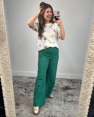 Woman taking a mirror selfie wearing a white floral top and green pants.