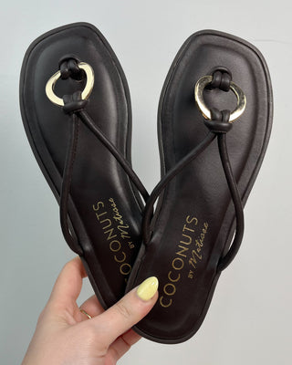 Pair of black sandals with gold accents held by a hand against a gray background