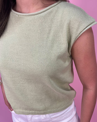 Person wearing a light green knitted top against a pink background