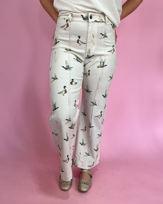 Person wearing white pants with duck pattern on a pink background