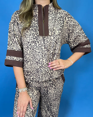 A woman modeling a matching two-piece leopard print lounge set with brown trim