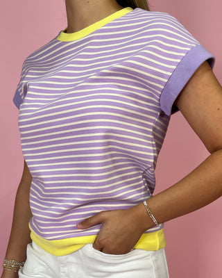 Person wearing a purple and white striped shirt with yellow accents on a pink background