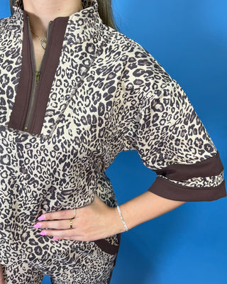 A woman modeling a matching two-piece leopard print lounge set with brown trim