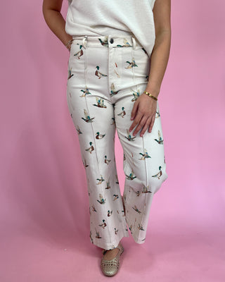 Person wearing white pants with duck pattern against a pink background