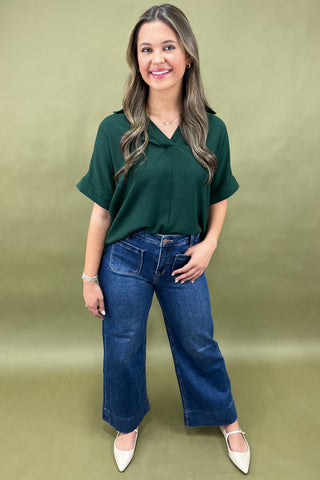 Woman wearing a green top and blue jeans against a green background