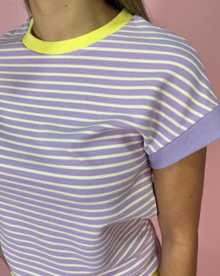 Person wearing a purple and yellow striped shirt against a pink background