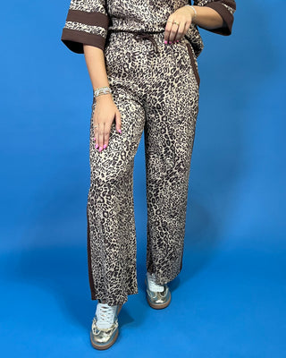 A woman modeling a matching two-piece leopard print lounge set with brown trim