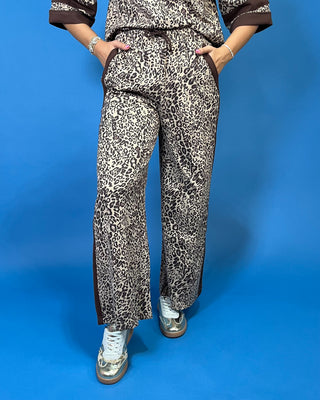 A woman modeling a matching two-piece leopard print lounge set with brown trim