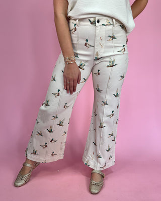 Person wearing white pants with duck pattern against a pink background