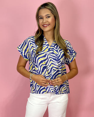 Woman wearing a blue and yellow patterned top with white pants on a pink background