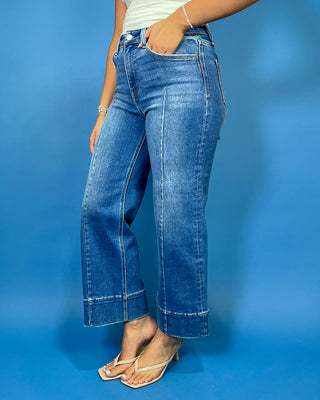 Medium wash high-rise cropped wide leg jeans with front seam detailing, subtle fading, a wide cuffed hem, and small front hem slits.