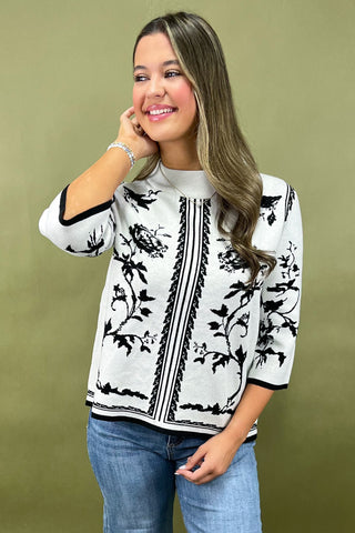 Woman wearing a white blouse with black floral patterns on a green background