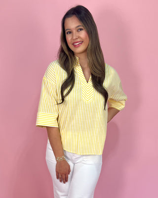 Woman wearing a yellow striped shirt and white pants against a pink background