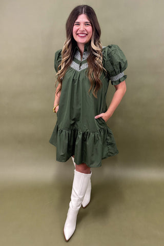 Woman wearing a green dress with white boots against a beige background