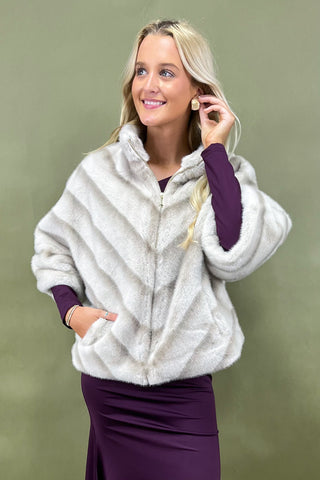 Woman wearing a white fur-like jacket over a purple outfit against a green background