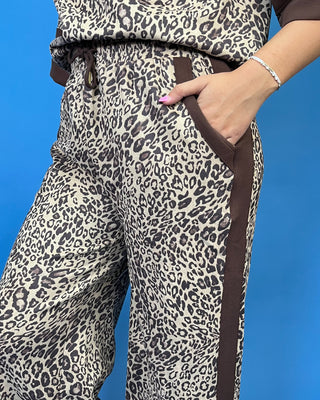 A close-up of a person wearing leopard-print pants with solid brown side panels and pocket trim