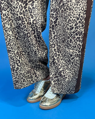 A woman modeling a matching two-piece leopard print lounge set with brown trim