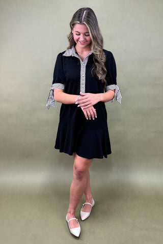 Woman wearing a black dress with white and gray striped sleeves against a plain background