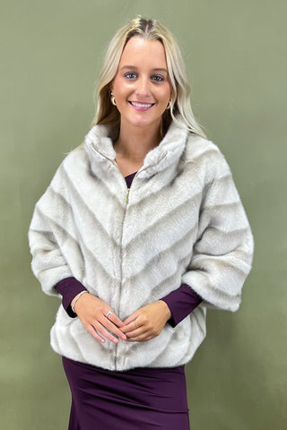 Woman wearing a white fur coat with purple sleeves against a green background