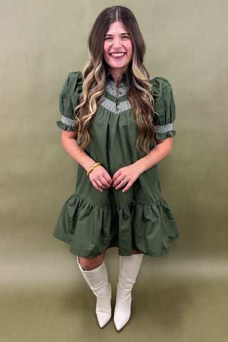 Woman wearing a green dress with white boots against a beige background