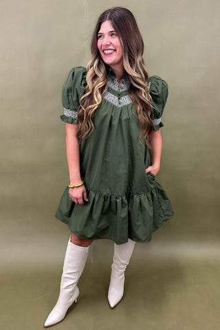 Woman wearing a green dress with white boots against an olive green background