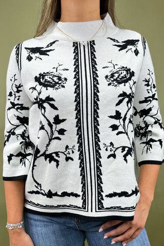White blouse with black floral patterns worn by a person on a green background