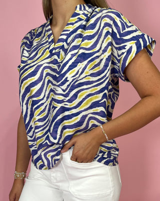 Person wearing a blue and yellow patterned top with white pants on a pink background