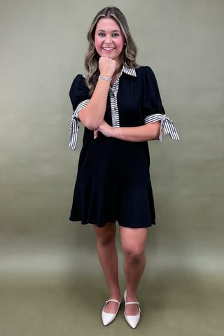 Woman wearing a black dress with striped sleeves against a green background
