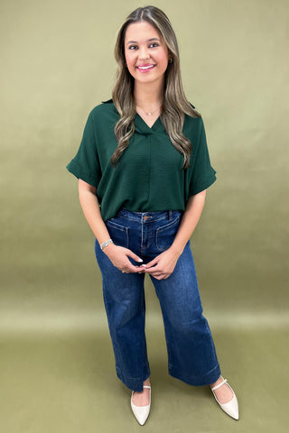 Woman wearing a green top and blue jeans against a green background
