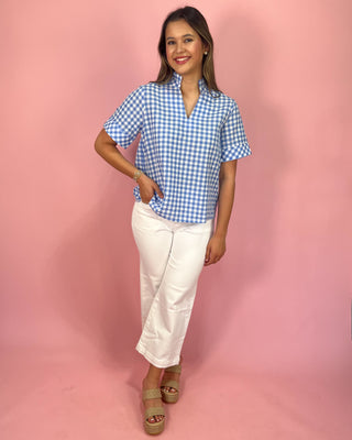 Woman wearing a blue checkered shirt and white pants on a pink background